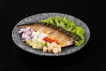 Fresh mackerel fillet served with chopped vegetables on a stone plate, isolated on a black background.