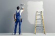 © antusher - Painter standing on ladder painting wall with roller, gray background with copy space