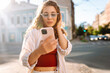 © maxbelchenko - Young woman enjoying a sunny day while using her smartphone on a vibrant urban street surrounded by classic architecture. Technology, blogging, communication concept.
