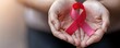 © Fokasu Art - Hands cupping a glowing red ribbon, symbolizing protection and care for HIV patients, World AIDS Day focus