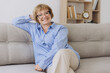 © anatoliycherkas - Smiling senior blonde haired woman looking at camera, happy old lady in glasses posing at home indoor, positive single senior retired female sitting on sofa in living room headshot portrait
