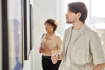 minimal side view portrait of man looking at paintings while visiting modern art gallery exhibition 