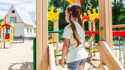 Cute child girl having fun on a playground outdoors in summer in sunny weather. Sport activities for kids.