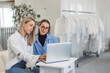 © VisualProduction - Two women collaborating on a laptop in a bright, modern workspace. One woman has long blonde hair and wears a white shirt, while the other has brown hair and glasses, dressed in a blue striped shirt.
