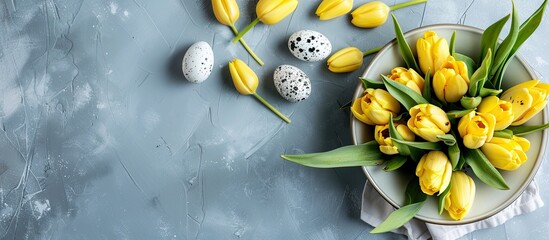 Wall Mural - A bouquet of fresh yellow tulips in a white jug with a gray plate featuring decorated Easter eggs on a blue background. with copy space image. Place for adding text or design