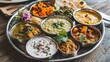 © วรรณภา มะโนศรี - A colorful thali featuring a variety of Indian dishes such as dal, vegetable curry, raita, and chapati, arranged on a traditional stainless steel platter.