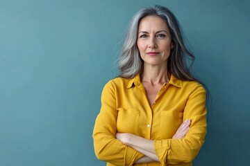 Beautiful, attractive, middle aged woman wearing casual yellow shirt with arms crossed standing isolated on blue background. with generative ai