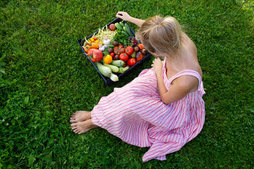 Modern young girl sitting on the lawn holding a basket with fresh vegetables