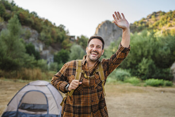 Portrait of adult man stand in front tent and wear backpack