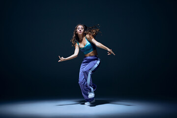 Canvas Print - Dynamic image of young girl, dancer showing technique during focused hip hop training session against navy blue studio background. Concept of freestyle dance, modernity, urban culture, youth