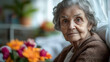 © Earny - An elderly woman sits by the window, surrounded by vibrant flowers, embodying wisdom and warmth in a cozy setting.