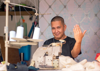 A friendly middle aged asian tailor smiling and inviting a customer to come inside his modest shop. A small business owner.