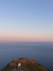 Poster - A small building sits atop a grassy hill overlooking the vast expanse of ocean.