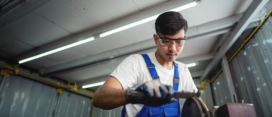 Canvas Print - A man in a blue vest is working on a machine. He is wearing safety glasses and gloves