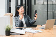 © kenchiro168 - A businesswoman smiling while video calling on her smartphone in an office setting
