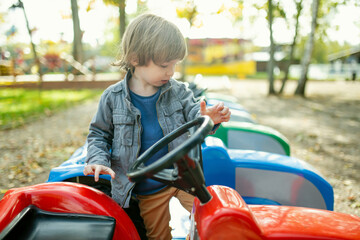 Cute toddler boy riding toy car having fun on a playground outdoors on warm autumn day.