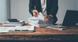 © Kritdanai - Overwhelmed by Paperwork: A businesswoman grapples with a towering stack of documents, her desk cluttered with the tools of a demanding profession, evoking the stress of deadlines and administrative o