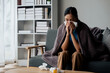 © aksonsat - Woman is ill sick with fever, a runny nose and cough feeling under weather under blanket in the living room at home and wipe a nose with facial tissue.