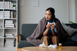 © aksonsat - Woman is ill sick with fever, a runny nose and cough feeling under weather under blanket in the living room at home and wipe a nose with facial tissue.