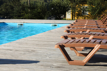 Poster - Empty sun loungers on wooden deck near outdoor swimming pool