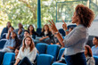 © SejutaCahaya - A young woman speaker with a microphone delivers a presentation to a large group of students.