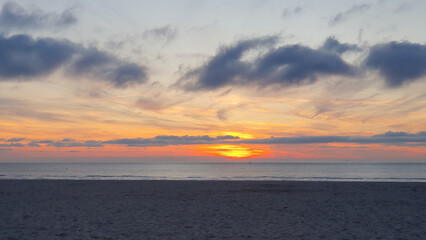 Beach at sunset in the evening. Much sand, water and clouds.