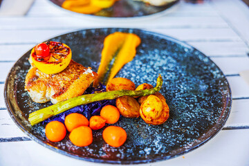 Beautiful close-up view of gourmet dish with grilled fish, roasted vegetables, asparagus, and slice of lemon on textured plate. Curacao.