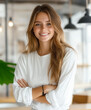 © Nano Photos - A person with long hair and a white shirt smiles confidently with arms crossed in a modern, well-lit room with hanging lights.
