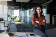 © Liubomir - Portrait of young beautiful Latin American business woman, company employee smiling and looking at camera with crossed arms, businesswoman satisfied with work inside office using laptop.