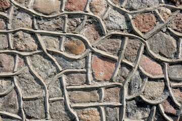 Fragment of a wall of an old building made of natural stones. There is a decorative finish of cement between individual boulders. Background. Close-up.