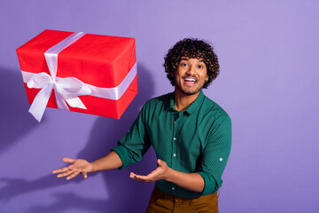 Wall Mural - Photo portrait of funny mexican guy with wavy haircut wearing casual shirt throwing red gift for new year isolated on violet color background