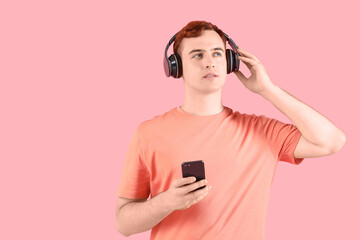 Sticker - Thoughtful young redhead man in headphones with mobile phone on pink background