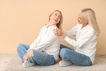 Canvas Print - Happy young beautiful woman with her mother sitting on floor near orange wall