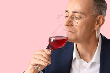 Wall Mural - Mature man tasting red wine on pink background, closeup