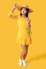 Poster - Beautiful young African-American woman with bouquet of gerbera flowers on yellow background. International Women's Day