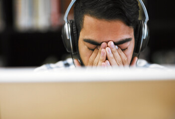 Poster - Man, university student and exhausted on computer with headphones in library for internet, online error and research. Male person, tired and burnout or headache with assignment deadline and study