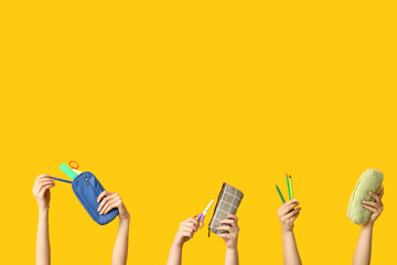 Wall Mural - Female hands with pencil cases and stationery on yellow background