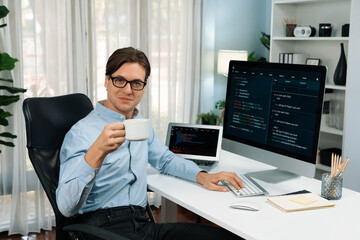 IT developer looking camera with holding coffee cup with online software on pc and laptop monitor beside, coding program on updated version application project creating new code system. Pecuniary.