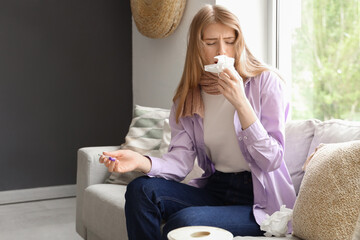 Canvas Print - Ill young woman with thermometer and tissue sneezing on sofa at home