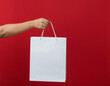 © sandor - Female hand holding a shopping bag. Red background.