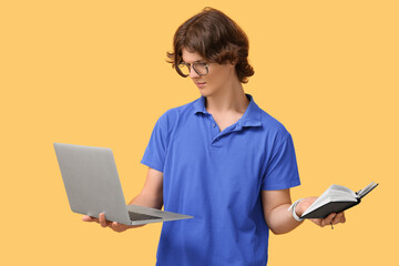 Wall Mural - Male programmer in eyeglasses with laptop and notebook on orange background