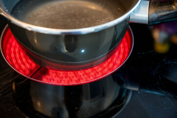 Close-up of a hob with electric hot plates: the heating elements are bright red,the pot of water placed on top is about to boil. Selective focus on the heating elements. Concept of energy consumption