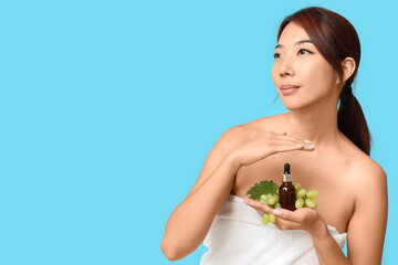 Canvas Print - Beautiful young Asian woman with bottle of cosmetic grape seed oil on blue background