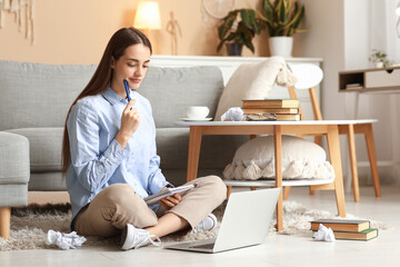 Wall Mural - Beautiful thoughtful female writer with laptop and notebook sitting on floor at home