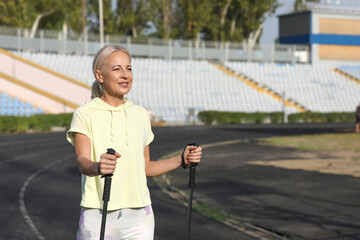 Canvas Print - Beautiful mature happy woman training with walking poles at stadium