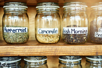 Container, jar and tea leaves on shelf at cafe for catering, organic flavor and drink in closeup. Collection, antioxidant and natural herbs with stock, inventory and label for beverage at coffee shop