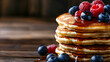© Komkrit - Close-up of a stack of golden-brown pancakes drenched in maple syrup, topped with fresh blueberries and raspberries, with a rustic wooden background