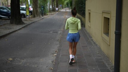 Wall Mural - A young woman is jogging energetically along a quiet street that is surrounded by lush greenery