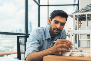 Wall Mural - Closeup portrait of smart caucasian architect engineer inspect house model while thinking about building construction at architect studio on table with project plan, blueprint, equipment. Tracery.