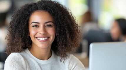 Canvas Print - A woman with curly hair is smiling and sitting in front of a laptop